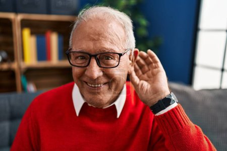 Téléchargez les photos : Homme âgé souriant confiant en utilisant l'aide auditive de surdité à la maison - en image libre de droit
