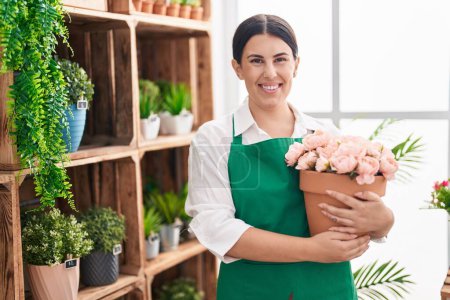 Photo for Young beautiful hispanic woman florist smiling confident holding plant at flower shop - Royalty Free Image