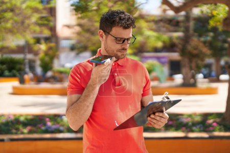 Téléchargez les photos : Jeune homme hispanique parlant sur le document de lecture smartphone au parc - en image libre de droit