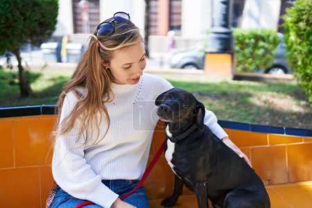 Téléchargez les photos : Jeune femme blonde souriante confiante assise sur le lit avec chien au parc - en image libre de droit