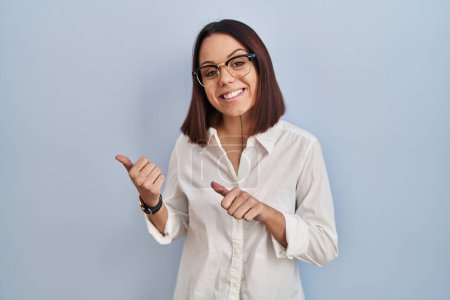 Téléchargez les photos : Young hispanic woman standing over white background pointing to the back behind with hand and thumbs up, smiling confident - en image libre de droit