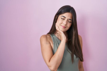 Foto de Mujer hispana de pie sobre fondo rosa tocando la boca con la mano con expresión dolorosa debido a dolor de muelas o enfermedad dental en los dientes. dentista - Imagen libre de derechos