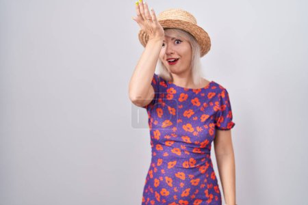 Foto de Mujer joven caucásica con vestido de flores y sombrero de verano sorprendido con la mano en la cabeza por error, recordar el error. olvidado, mal concepto de memoria. - Imagen libre de derechos