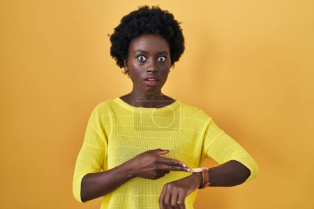 Téléchargez les photos : Jeune femme africaine debout au-dessus studio jaune pressé pointant pour regarder le temps, impatience, bouleversé et en colère pour retard de délai - en image libre de droit