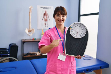 Photo for Young brunette woman as nutritionist holding weighing machine smiling happy pointing with hand and finger - Royalty Free Image