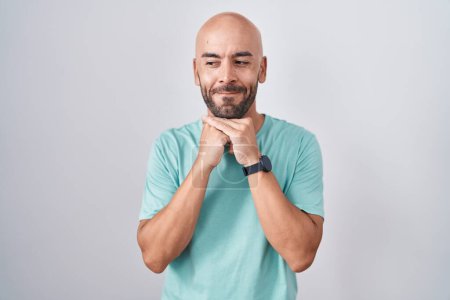 Foto de Middle age bald man standing over white background laughing nervous and excited with hands on chin looking to the side - Imagen libre de derechos