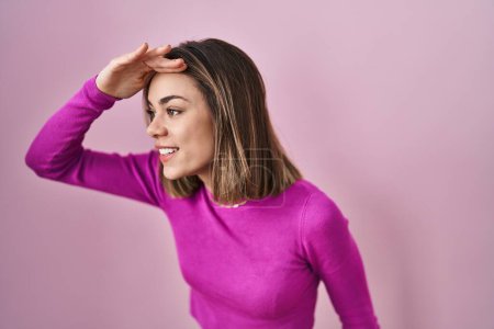Photo for Hispanic woman standing over pink background very happy and smiling looking far away with hand over head. searching concept. - Royalty Free Image
