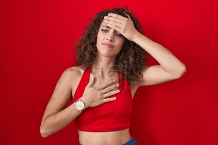 Photo for Hispanic woman with curly hair standing over red background touching forehead for illness and fever, flu and cold, virus sick - Royalty Free Image