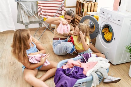 Photo for Mother and daughters smiling confident fighting with clothes at laundry room - Royalty Free Image