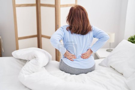 Téléchargez les photos : Senior woman suffering for backache sitting on bed at bedroom - en image libre de droit