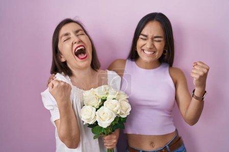 Photo for Hispanic mother and daughter holding bouquet of white flowers very happy and excited doing winner gesture with arms raised, smiling and screaming for success. celebration concept. - Royalty Free Image