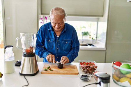 Photo for Senior man smiling confident cutting avocado at kitchen - Royalty Free Image