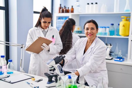 Téléchargez les photos : Three woman scientists using microscope write on checklist at laboratory - en image libre de droit