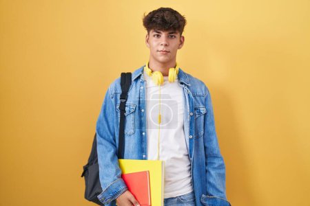 Photo for Hispanic teenager wearing student backpack and holding books relaxed with serious expression on face. simple and natural looking at the camera. - Royalty Free Image