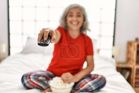 Photo for Middle age grey-haired woman watching movie sitting on the bed at bedroom. - Royalty Free Image