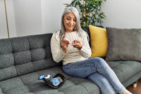 Téléchargez les photos : Middle age grey-haired woman smiling confident measuring glucose at home - en image libre de droit