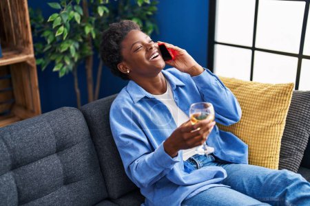 Foto de Mujer afroamericana hablando en el teléfono inteligente bebiendo champán en casa - Imagen libre de derechos