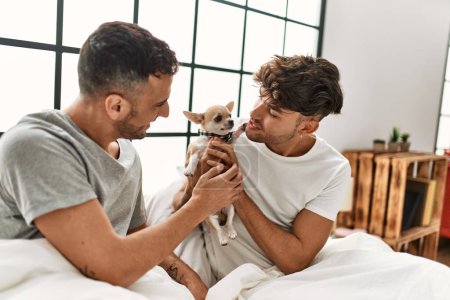 Photo for Two hispanic men couple sitting on bed with chihuahua at bedroom - Royalty Free Image
