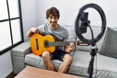 Photo for Young hispanic man having online concert playing classical guitar at home - Royalty Free Image