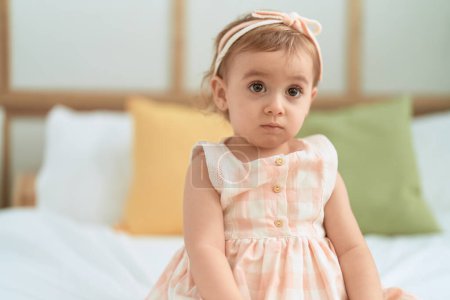 Téléchargez les photos : Adorable fille caucasienne assise sur le lit avec une expression détendue dans la chambre - en image libre de droit