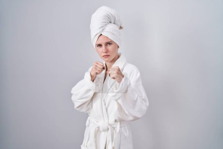 Photo for Blonde caucasian woman wearing bathrobe punching fist to fight, aggressive and angry attack, threat and violence - Royalty Free Image