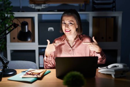 Photo for Middle age hispanic woman working using computer laptop late at night looking confident with smile on face, pointing oneself with fingers proud and happy. - Royalty Free Image