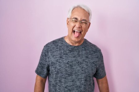 Foto de Middle age man with grey hair standing over pink background sticking tongue out happy with funny expression. emotion concept. - Imagen libre de derechos