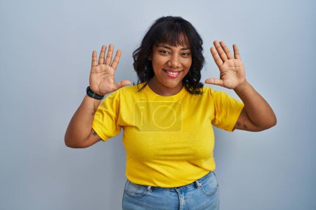 Foto de Hispanic woman standing over blue background showing and pointing up with fingers number ten while smiling confident and happy. - Imagen libre de derechos