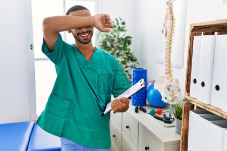 Photo for African american physiotherapist man working at pain recovery clinic smiling cheerful playing peek a boo with hands showing face. surprised and exited - Royalty Free Image
