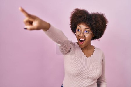 Foto de Young african american woman standing over pink background pointing with finger surprised ahead, open mouth amazed expression, something on the front - Imagen libre de derechos