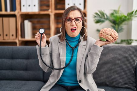 Photo for Middle age hispanic woman working at therapy office holding brain clueless and confused expression. doubt concept. - Royalty Free Image
