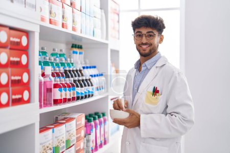 Téléchargez les photos : Jeune homme arabe pharmacien souriant confiant travaillant à la pharmacie - en image libre de droit