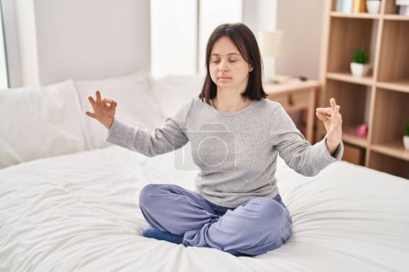 Téléchargez les photos : Jeune femme avec le syndrome du duvet faire de l'exercice de yoga assis sur le lit dans la chambre - en image libre de droit