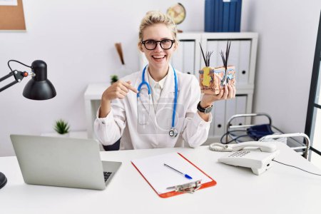 Photo for Young doctor woman holding model of human anatomical skin and hair at the clinic pointing finger to one self smiling happy and proud - Royalty Free Image