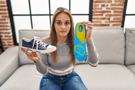 Photo for Young woman holding shoe insole skeptic and nervous, frowning upset because of problem. negative person. - Royalty Free Image