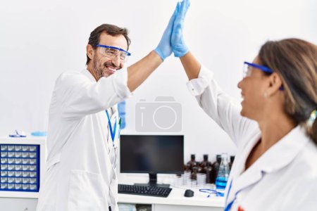 Foto de Middle age man and woman partners wearing scientist uniform high five with hands raised up at laboratory - Imagen libre de derechos