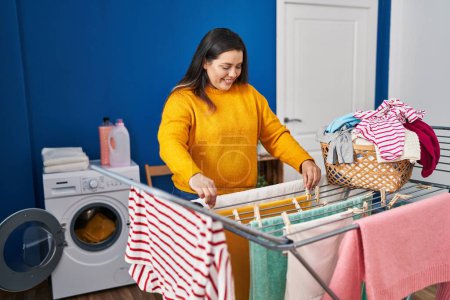 Photo for Young beautiful plus size woman smiling confident hanging clothes on clothesline at laundry room - Royalty Free Image