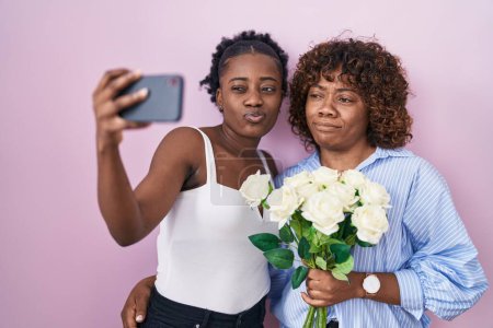 Téléchargez les photos : Two african women taking a selfie photo with flowers smiling looking to the side and staring away thinking. - en image libre de droit