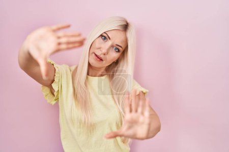 Téléchargez les photos : Femme blanche debout sur fond rose faisant cadre en utilisant les mains paumes et les doigts, perspective de la caméra - en image libre de droit