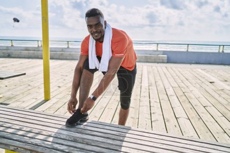Photo for Young african american man wearing sportswear tying shoe at seaside - Royalty Free Image