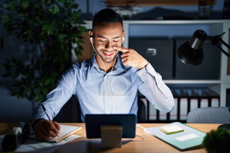 Foto de Young hispanic man working at the office at night pointing with hand finger to face and nose, smiling cheerful. beauty concept - Imagen libre de derechos