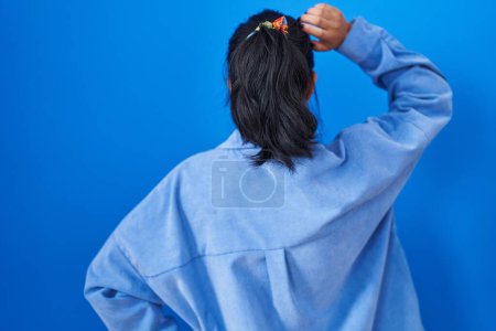 Foto de Asiática joven de pie sobre fondo azul hacia atrás pensando en la duda con la mano en la cabeza - Imagen libre de derechos
