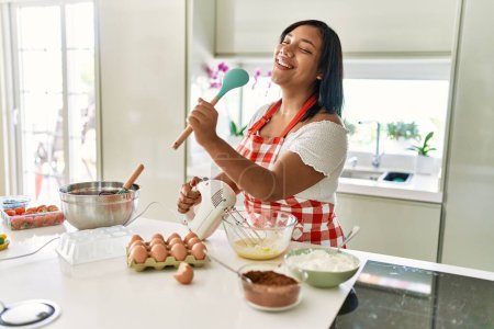 Photo for Hispanic brunette woman preparing cake dancing at singing at the kitchen - Royalty Free Image