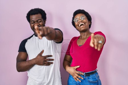 Téléchargez les photos : Jeune couple afro-américain debout sur fond rose se moquant de vous, pointant du doigt la caméra avec la main sur le corps, expression de honte - en image libre de droit