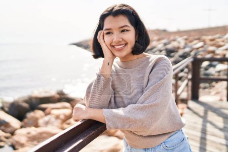 Téléchargez les photos : Jeune femme souriant confiant regardant sur le côté à la mer - en image libre de droit