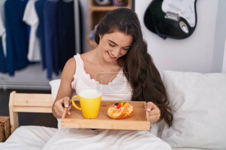 Téléchargez les photos : Young hispanic woman having breakfast sitting on bed at bedroom - en image libre de droit