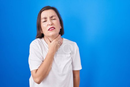 Photo for Middle age hispanic woman standing over blue background touching painful neck, sore throat for flu, clod and infection - Royalty Free Image