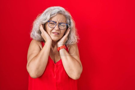 Photo for Middle age woman with grey hair standing over red background covering ears with fingers with annoyed expression for the noise of loud music. deaf concept. - Royalty Free Image
