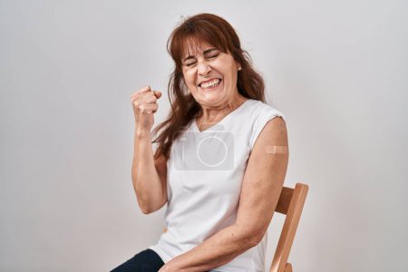 Téléchargez les photos : Middle age hispanic woman getting vaccine showing arm with band aid very happy and excited doing winner gesture with arms raised, smiling and screaming for success. celebration concept. - en image libre de droit