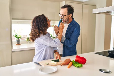 Photo for Middle age hispanic couple smiling confident eating zucchini at kitchen - Royalty Free Image